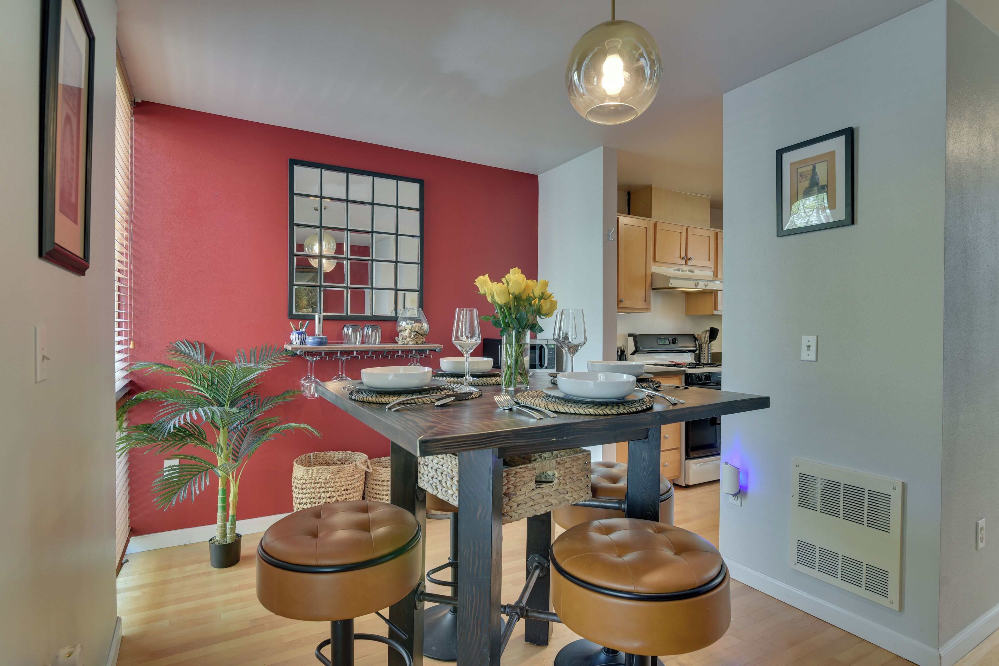 A dining area with a wooden table, two leather stools, a vase with yellow flowers, and a hanging light fixture.