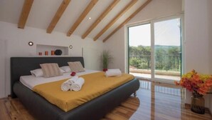 A bedroom with a large bed, wooden beams, a sliding glass door, and a view of greenery. - Villa P - Holiday Home (Sibenik)