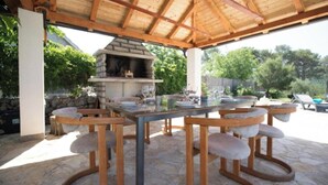 An outdoor patio with a stone table, bar stools, and a stone oven. - Villa P - Holiday Home (Sibenik)