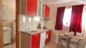 A compact kitchen with a sink, a small dining area with a table and chairs, and red and white cabinetry. - Apartments Clementina Sunrise-standard Studio Apartment (Orebic)