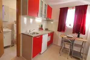 Eine kompakte Küche mit Spüle, einer kleinen Essecke mit Tisch und Stühlen sowie roten und weißen Schränken.