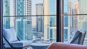 A modern hotel room with a large window overlooking a cityscape of high-rise buildings. - Marina Living Residences - Dubai Marina (Dubai)