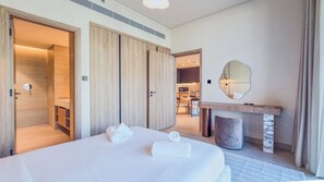 A hotel room with a large bed, a wooden wardrobe, a bathroom, a dining area, and a mirror on the wall. - Marina Living Residences - Dubai Marina (Dubai)