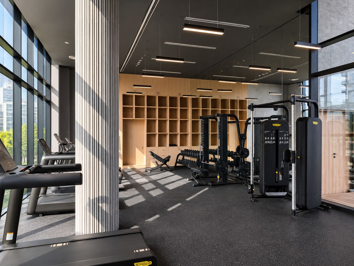 A modern gym with treadmills, weight machines, and a wall of shelves.