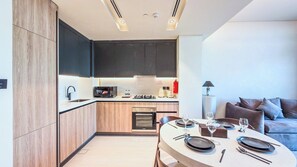 A modern kitchen with built-in appliances, a dining area with a round table set for two, and a sofa in the adjacent living space. - Marina Living Residences - Dubai Marina (Dubai)
