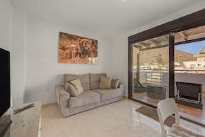 A living room with a beige sofa, a television, and a large window overlooking a residential area.