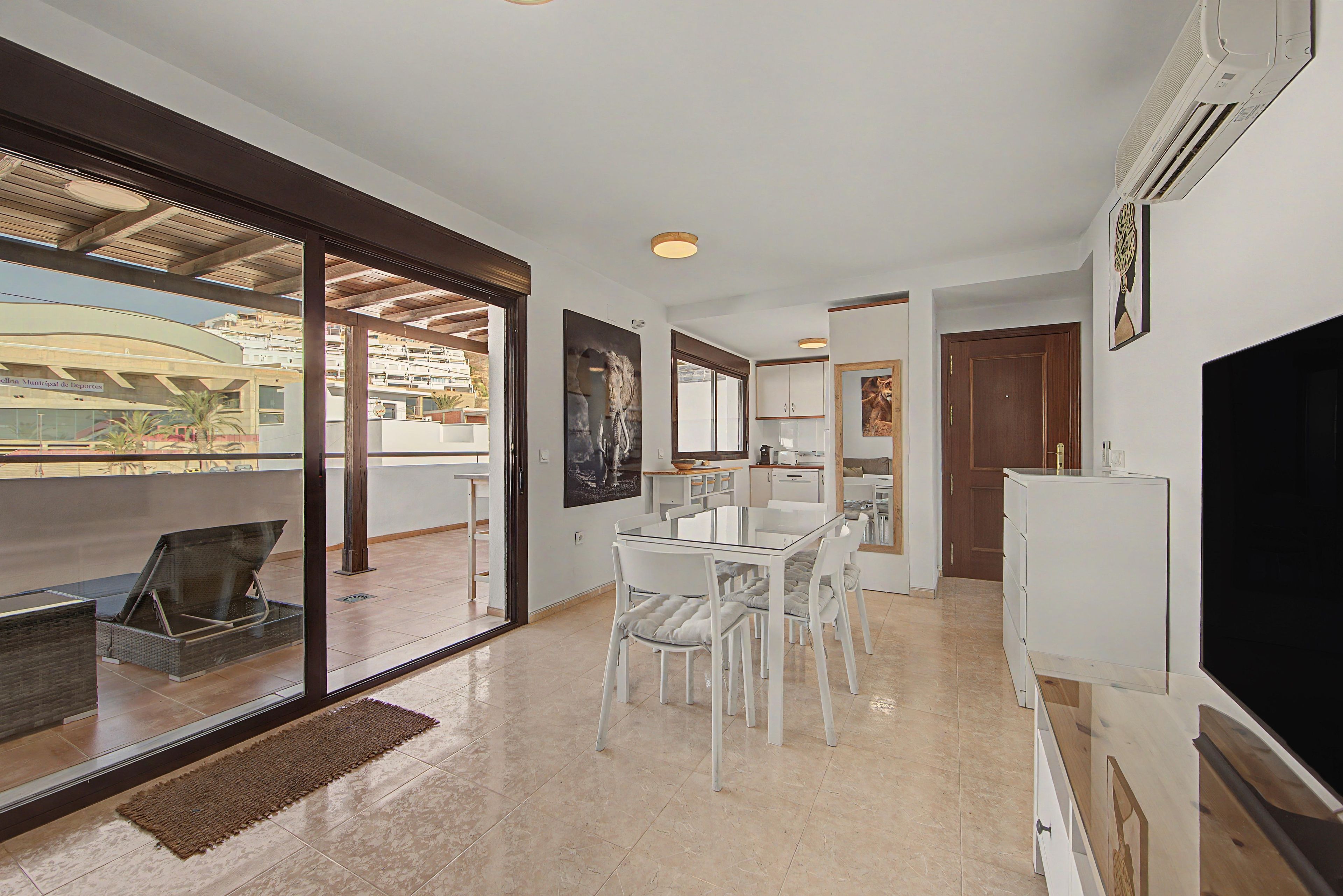 A modern interior with a dining area, kitchen, and a large window overlooking a building.