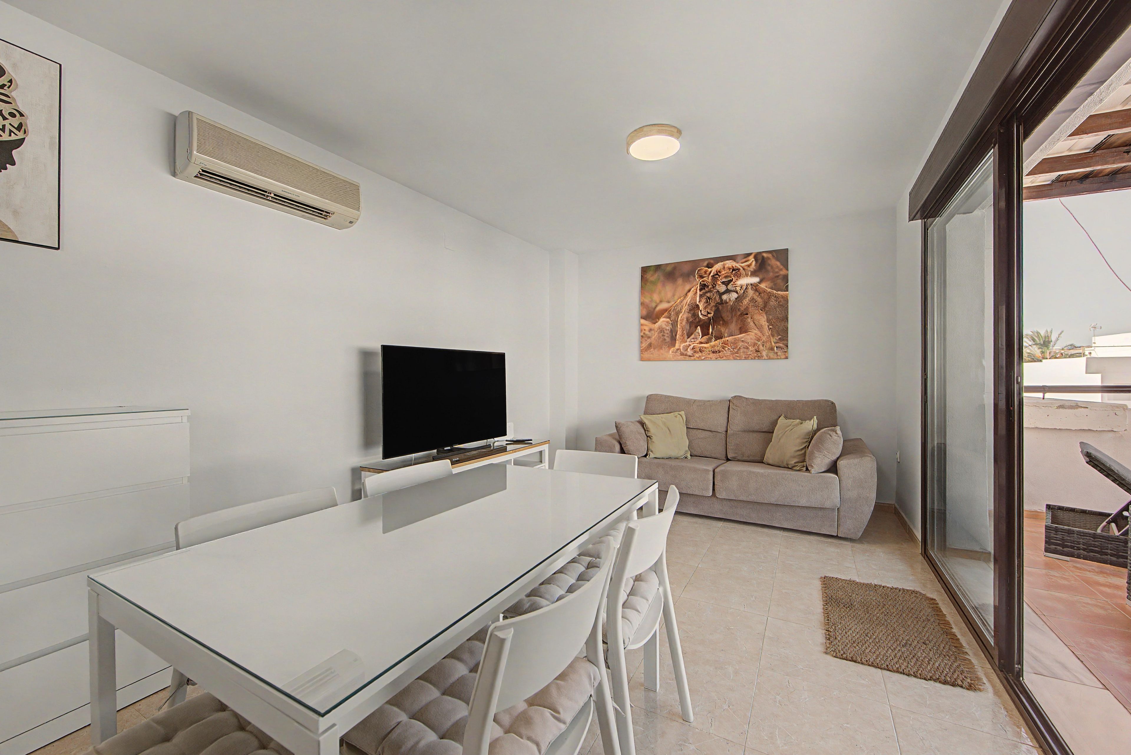 Een moderne woonkamer met een flatscreen televisie, een beige bank en een groot raam.