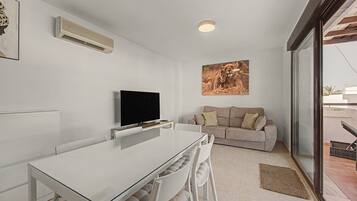 Een moderne woonkamer met een flatscreen televisie, een beige bank en een groot raam.