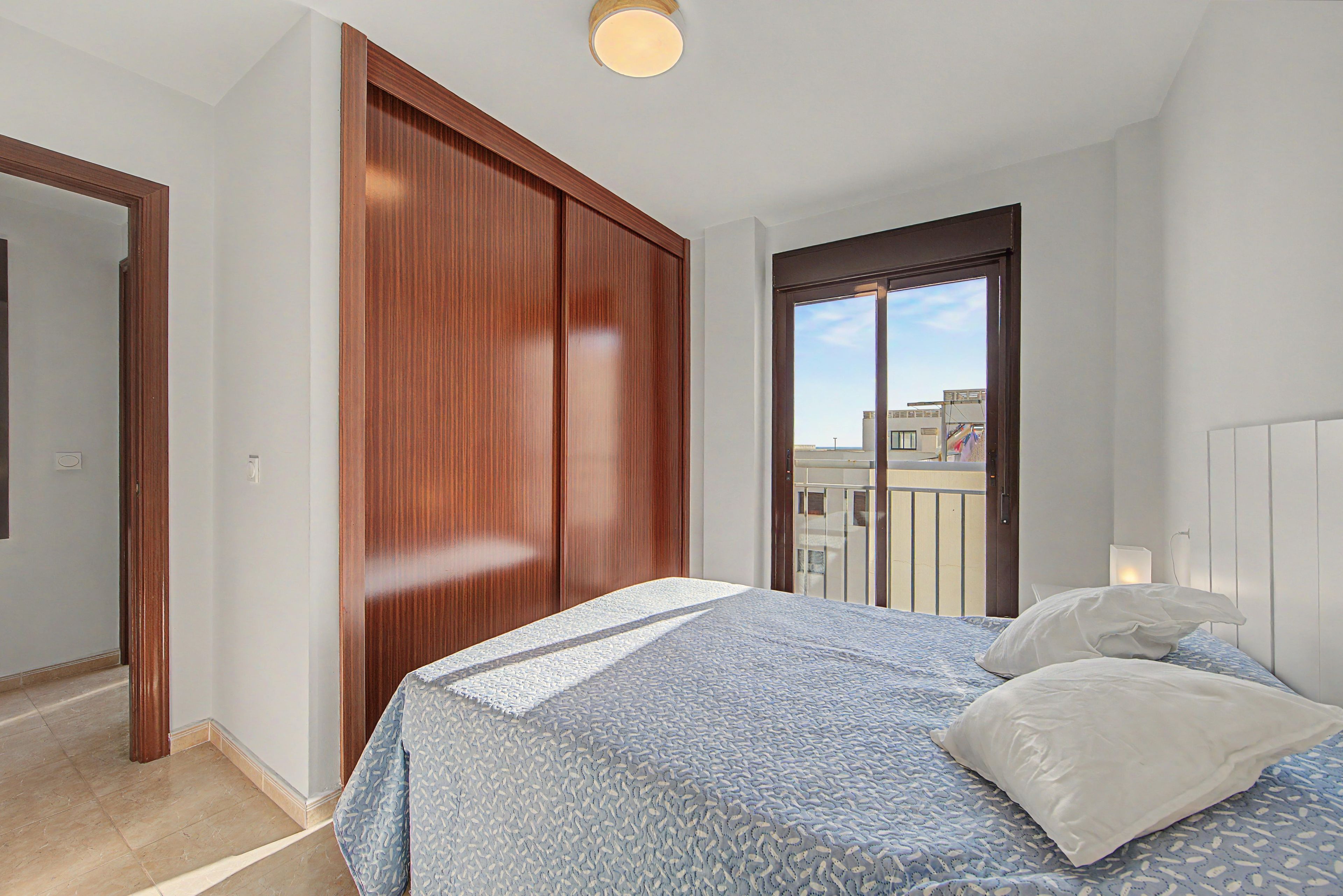 A bedroom with a bed, a wooden wardrobe, and a balcony door.