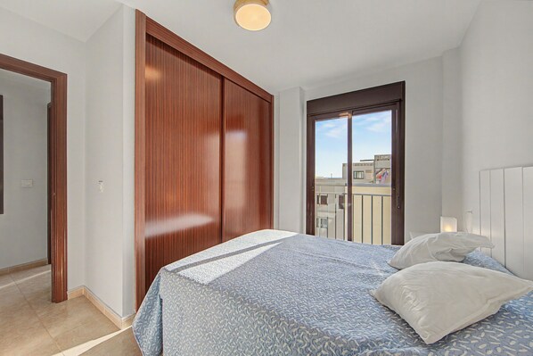 A bedroom with a bed, a wooden wardrobe, and a balcony door.