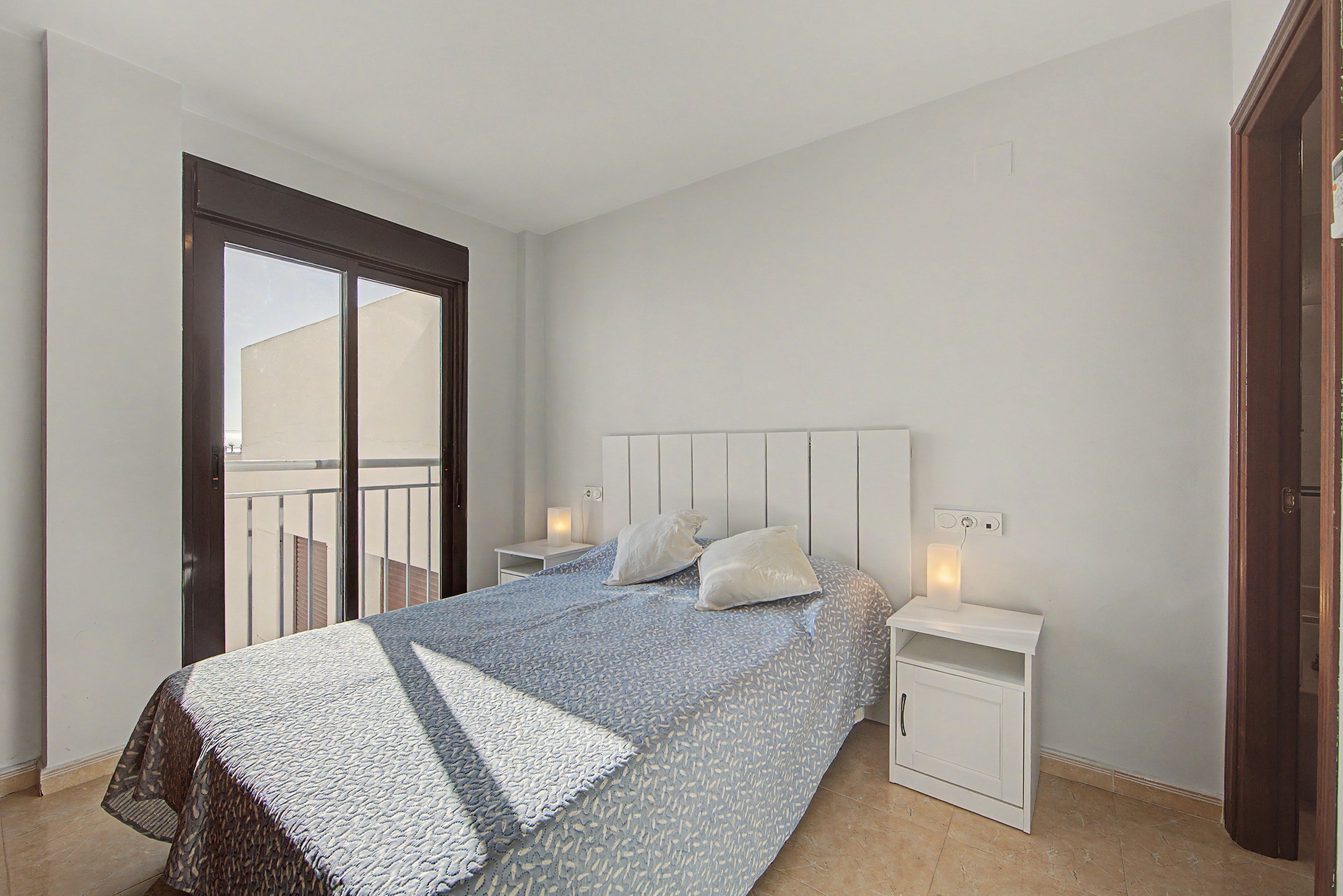 Une chambre à coucher comprenant un lit, des tables de chevet, une armoire et une porte coulissante donnant sur le balcon.