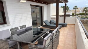 Un patio al aire libre con una mesa de vidrio, sillas de mimbre y sillones.