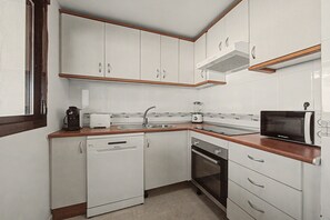 A compact kitchen with white cabinets, a dishwasher, an oven, a microwave, and a coffee maker.