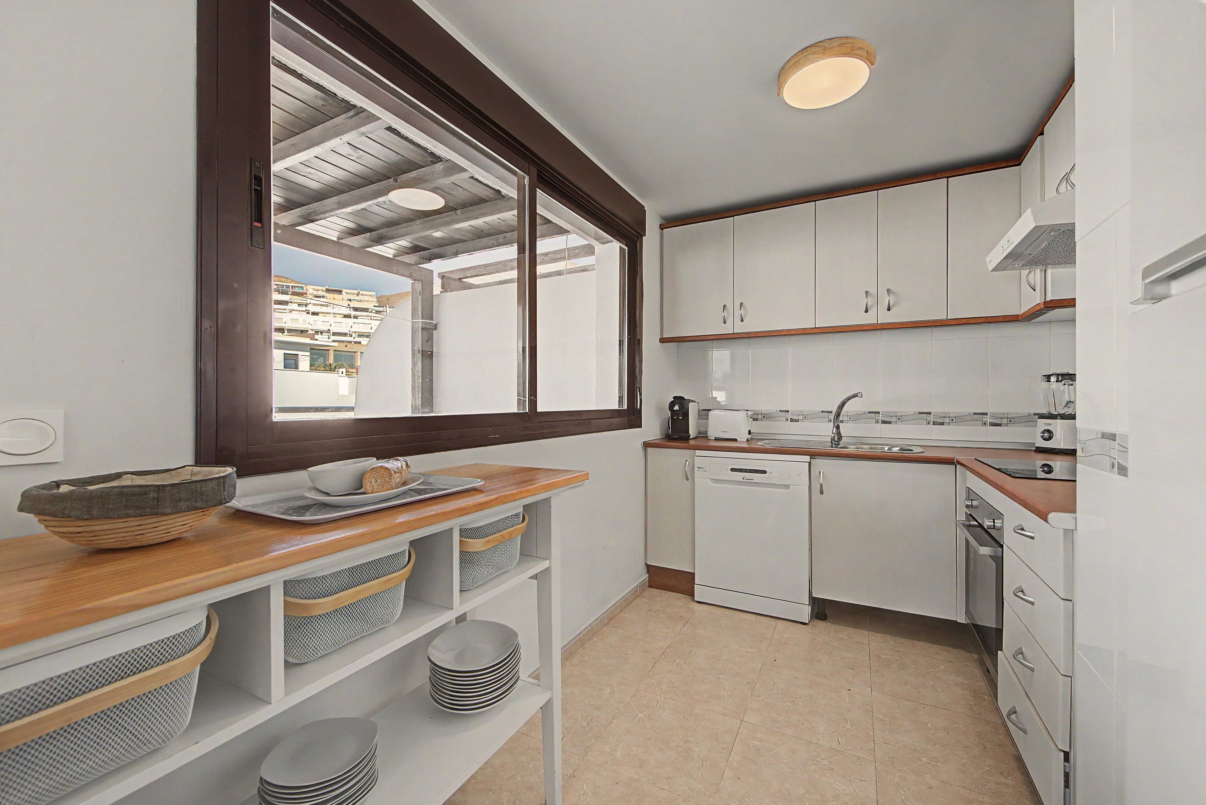 A compact kitchen with white cabinets, a wooden countertop, and a view of a residential area through a large window.