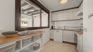 A compact kitchen with white cabinets, a wooden countertop, and a view of a residential area through a large window.
