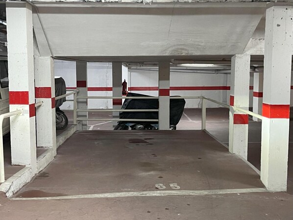 A parking garage with concrete pillars, a ramp leading to a parking area, and a fire extinguisher mounted on a pillar.