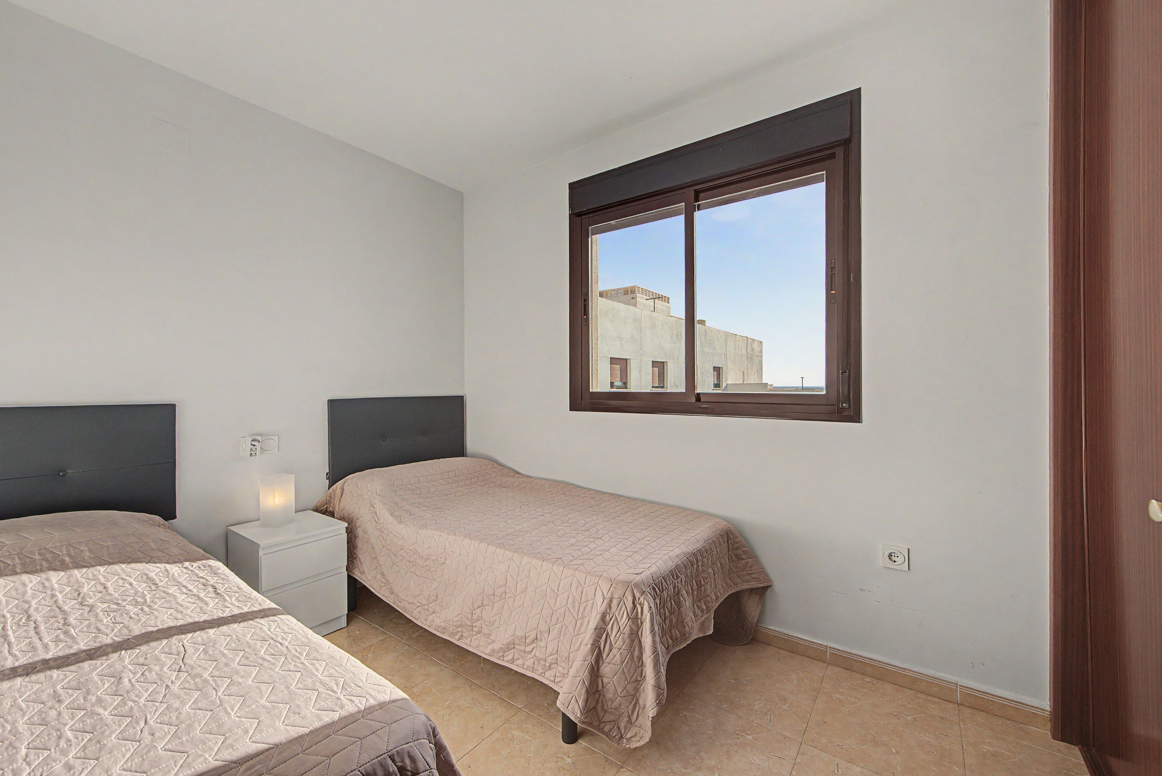 Un dormitorio con dos camas, una mesita de noche, un ventanal con vistas a edificios y una puerta.