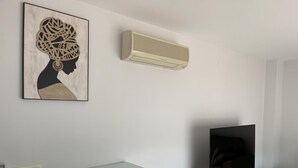 Una sala de estar moderna con un televisor de pantalla plana sobre un mueble de madera, un aire acondicionado instalado en la pared y una obra de arte enmarcada sobre el mueble.