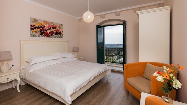 Un dormitorio con cama, mesita de noche, lámpara, un cuadro, puerta al balcón y vistas al exterior.