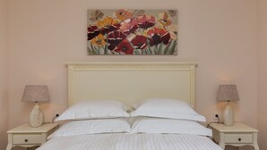 Una cama con ropa blanca, dos mesitas de noche con lámparas y un cuadro floral en la pared.