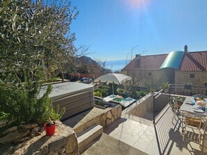 A terrace with a stone bench, a table with chairs, and a view of the sea. - Holiday Home Sunrise - Three Bedroom Holiday Home (Omis)