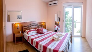 A bedroom with a bed, bedside tables, an air conditioning unit, a window, and a door. - Apartments Smokvica - Superior One Bed/ Apt (Starigrad)