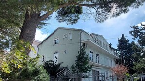 A multi-story building with a balcony on the second floor, surrounded by trees and a metal fence. - Apartments Smokvica - Superior One Bed/ Apt (Starigrad)