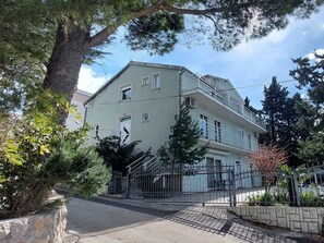 A multi-story building with a balcony on the second floor, surrounded by trees and a metal fence. - Apartments Smokvica - Superior One Bed/ Apt (Starigrad)