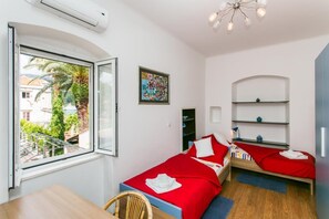 Ein Zimmer mit zwei Betten, einem Fenster, einem Bild und einer Deckenleuchte.