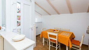 A dining area with a table set for two, chairs, a bowl of fruit, and a white counter with a plate. - Villa Marini Dvori - Two-bedroom Apartment With Terrace (Dubrovnik)