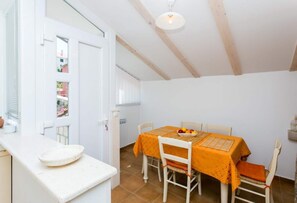Ein Essbereich mit einem Tisch für zwei Personen, Stühlen, einer Obstschale und einer weißen Arbeitsplatte mit einem Teller.