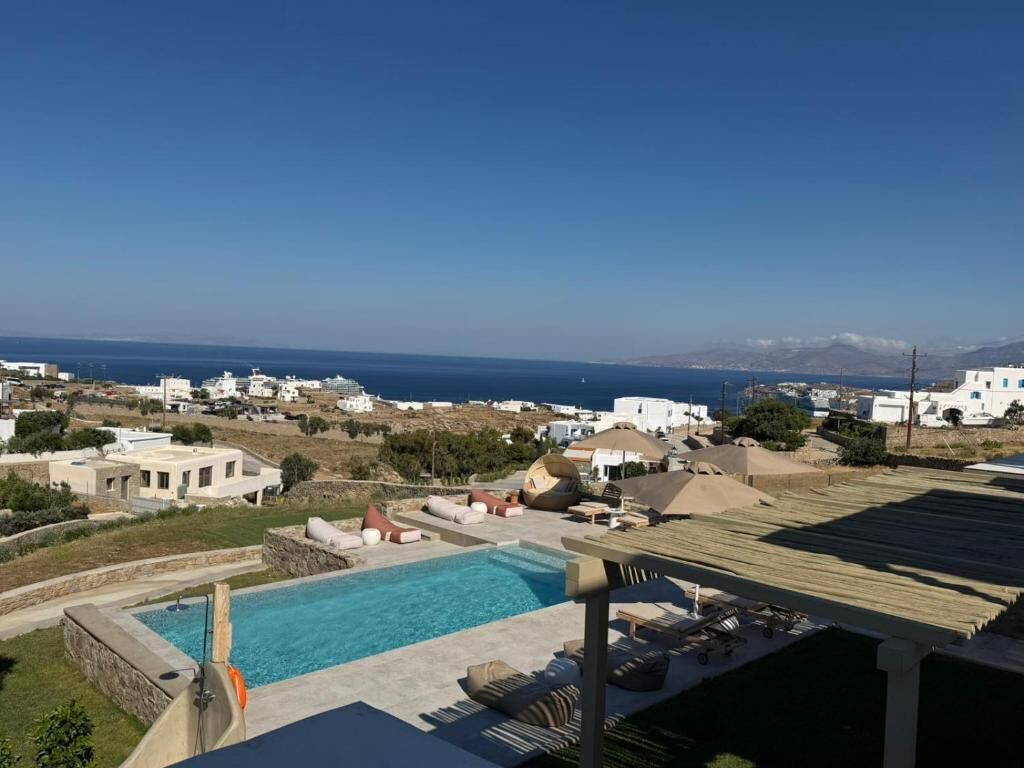 A pool area with a view of the sea and white buildings in the background.