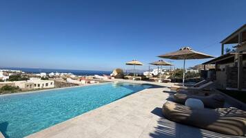 A swimming pool with lounge chairs and umbrellas, overlooking a coastal area.
