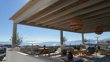 Una terraza con mesas al aire libre, vista al mar y cielo despejado.