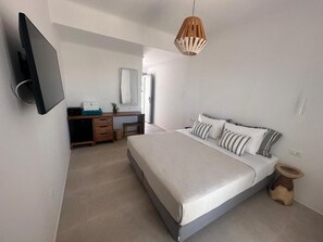 A bedroom with a bed, bedside table, lamp, and a TV mounted on the wall. - Ostria View Resort (Mykonos)