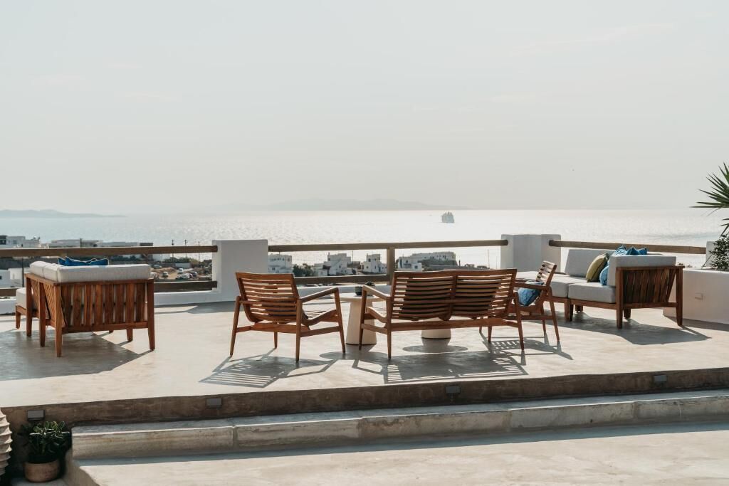 A rooftop terrace with outdoor seating, a view of the sea, and a distant cityscape.