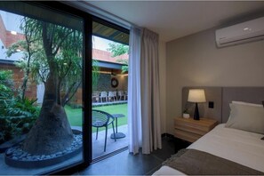A hotel room with a bed, a nightstand, a lamp, and a view of a garden through a glass door. - Casa Makech: Premium · ★ Largest Suite - Suite 3 (Zapopan)