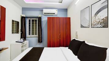 A hotel room with a bed, a desk, a wardrobe, a window with curtains, and artwork on the walls.
