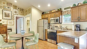A compact kitchen with a dining area, wooden cabinets, stainless steel appliances, and a wall adorned with framed pictures. - Walk to Waynesville Hot Spots! 'Woodland Cottage' (Waynesville)
