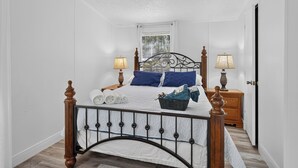 Een keurig opgemaakte slaapkamer met een bed, twee nachtkastjes, een raam en een deur.
