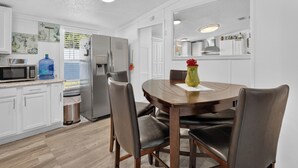 Een moderne keuken met witte kasten, een roestvrijstalen koelkast, een magnetron en een eettafel met stoelen.