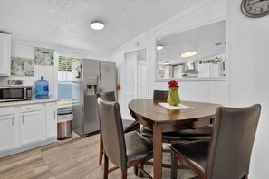 A modern kitchen with white cabinets, a stainless steel refrigerator, a microwave, and a dining table with chairs. - 6 Mi to Rainbow Springs! Home w/ Outdoor Space (Ocala)