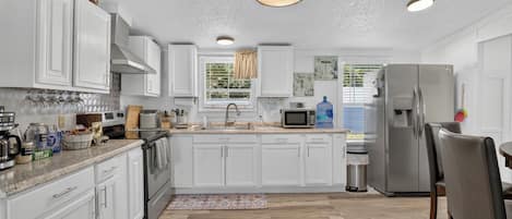 A modern kitchen with white cabinetry, a stainless steel refrigerator, a microwave, and a large water dispenser.