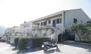 A building with a staircase leading to a balcony, a parked scooter, and a sign indicating rooms and a camera. - Guest House Bridge View - Studio With Balcony and Sea View (Dubrovnik)