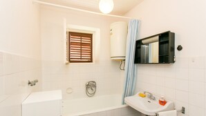 Ein Badezimmer mit einer Badewanne, einem Waschbecken, einem Fenster mit Jalousien, einem Handtuchhalter und einer Toilette.