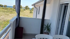 A covered balcony with a table and chairs, a potted plant, and a view of the sea. - Apartments Libertas - One Bedroom Apartment With Terrace and Sea View- (Rogoznica)