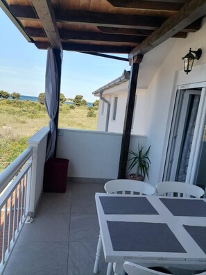 A covered balcony with a table and chairs, a potted plant, and a view of the sea. - Apartments Libertas - One Bedroom Apartment With Terrace and Sea View- (Rogoznica)