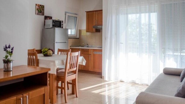 Eine moderne Küche mit Holzausstattung, einem Esstisch und Stühlen. Außerdem eine Couch und ein Fenster mit Vorhängen.