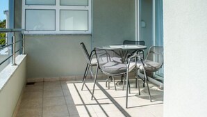 Ein Balkon mit gefliestem Boden, einer Glastür und einem Tisch mit Stühlen.